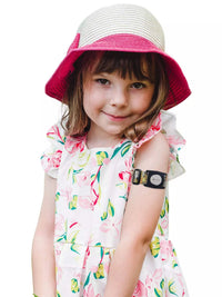 Child wearing Dexcom G7 Armband with rotating clip, playful design, floral dress, and pink hat.