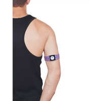 Person wearing a purple patterned Freestyle Libre 3 Arm Band on upper arm with sensor attached, visible from back and side view.
